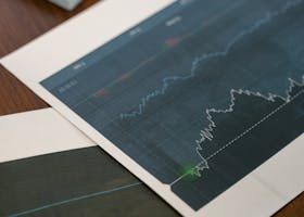 Papers with financial graphs beside stacks of US dollar bills representing market analytics.